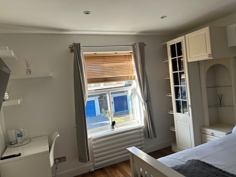 Bright bedroom with double bed, wooden flooring, window with blinds and curtains, white storage shelving