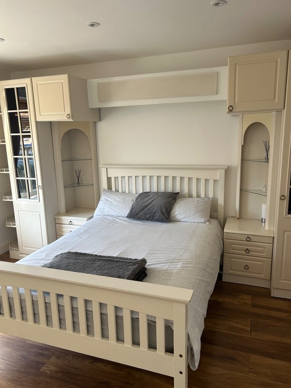 Cream bedroom with built-in wardrobes, double bed, grey cushion and wooden flooring