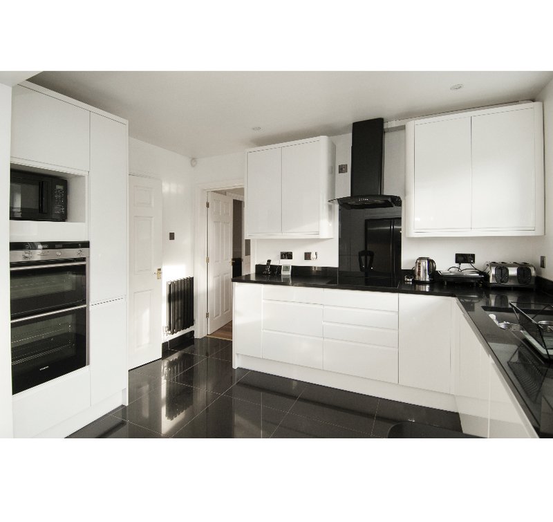 Modern kitchen with white cabinetry, black countertops, integrated appliances and black range hood