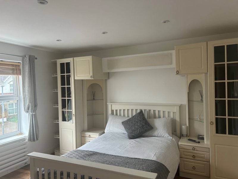 Bedroom with built-in cream wardrobe, single bed with white bedding, and window with curtains