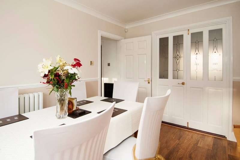 Modern dining room with white table, upholstered chairs, fresh flower arrangement, and glass-door cabinetry