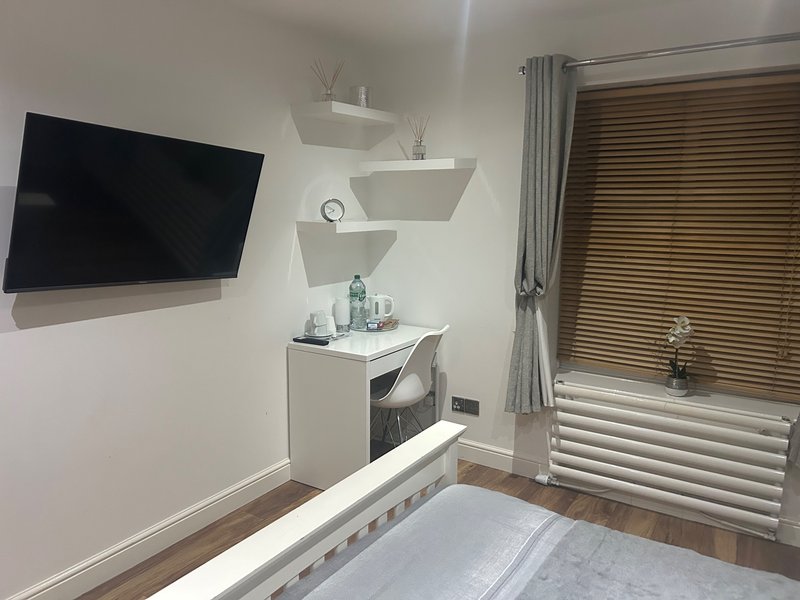 Bedroom with wall-mounted TV, floating shelves, desk, chair, and wooden floor