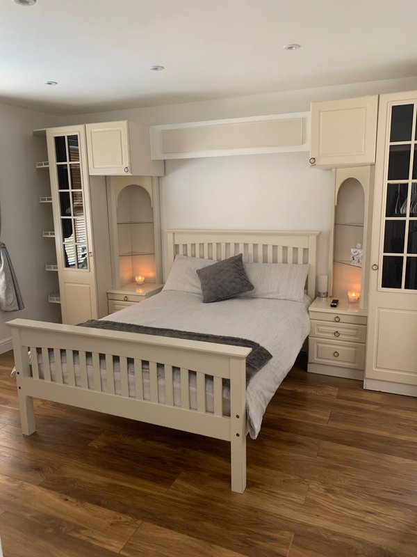 Spacious bedroom with cream wooden bed frame, built-in wardrobes, bedside lamps, and wooden flooring