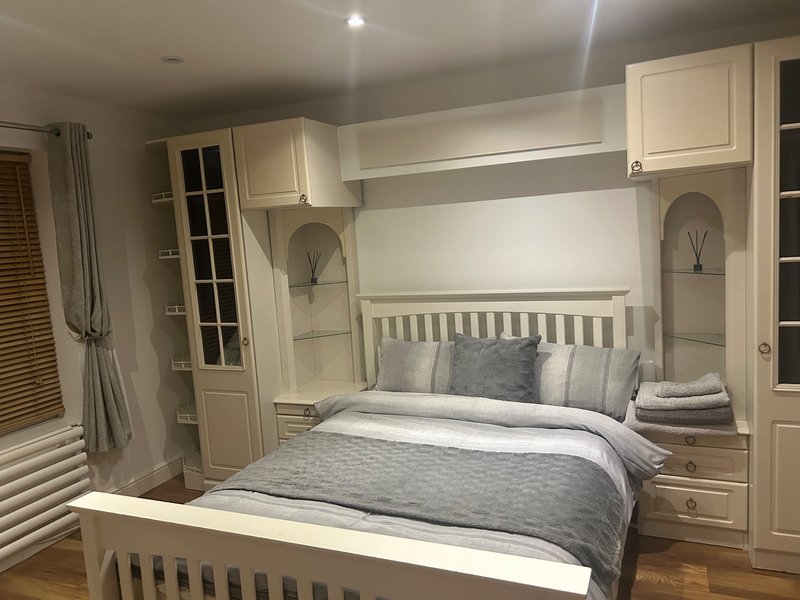 Modern bedroom with built-in cream cabinetry, grey and white bedding, and wooden flooring