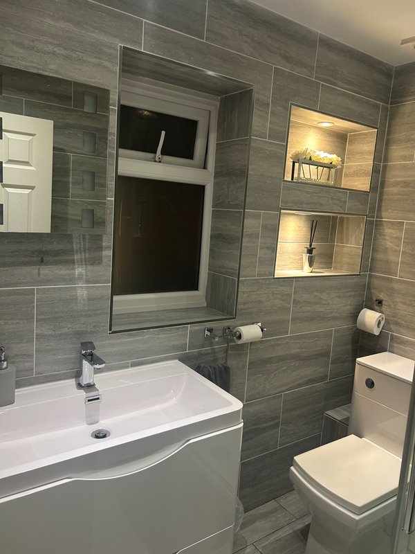 Modern bathroom with grey tile walls, white vanity sink, mirror, and toilet