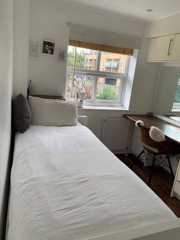 Single bedroom with white bed, desk, chair, and large window overlooking street