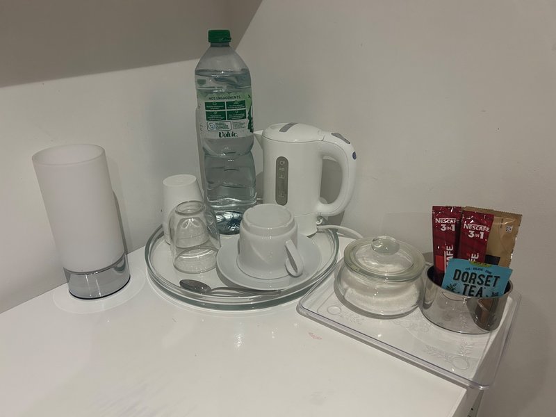 Hotel welcome tray with kettle, cups, water bottle, tea bags and toiletries on white surface