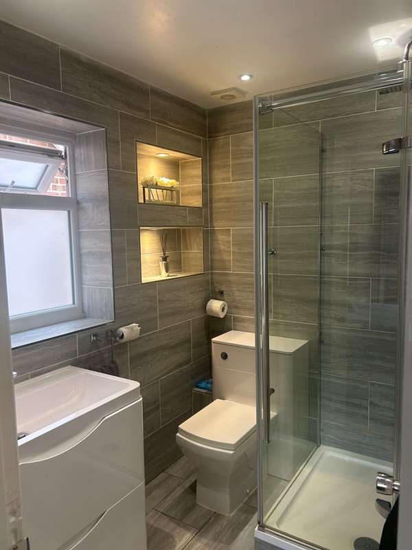 Modern bathroom with walk-in shower, toilet, sink and illuminated wall shelving