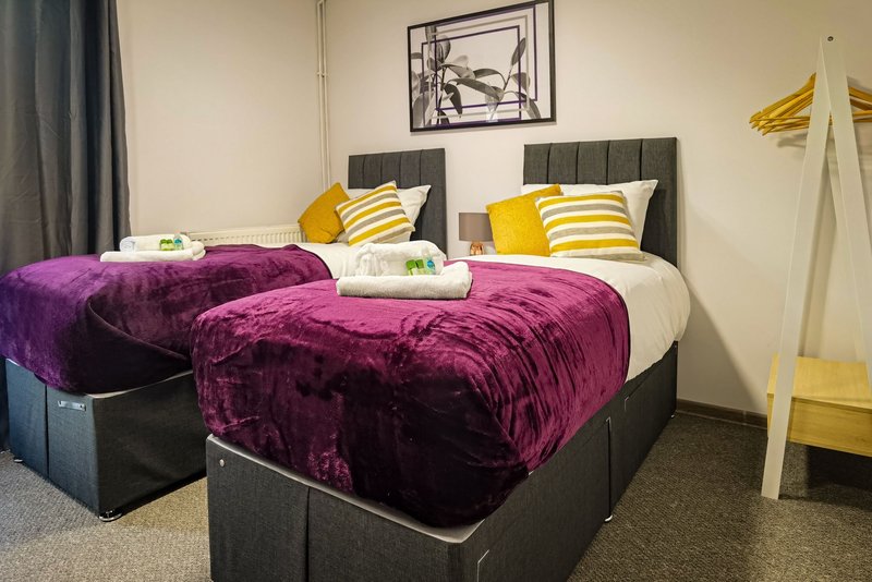 Twin bedroom with purple velvet bedspreads, yellow striped pillows and grey headboards
