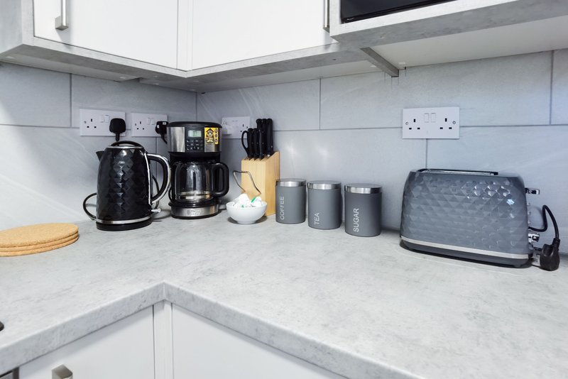 Modern kitchen corner with white cabinetry, marble countertop, and small appliances including kettle and toaster