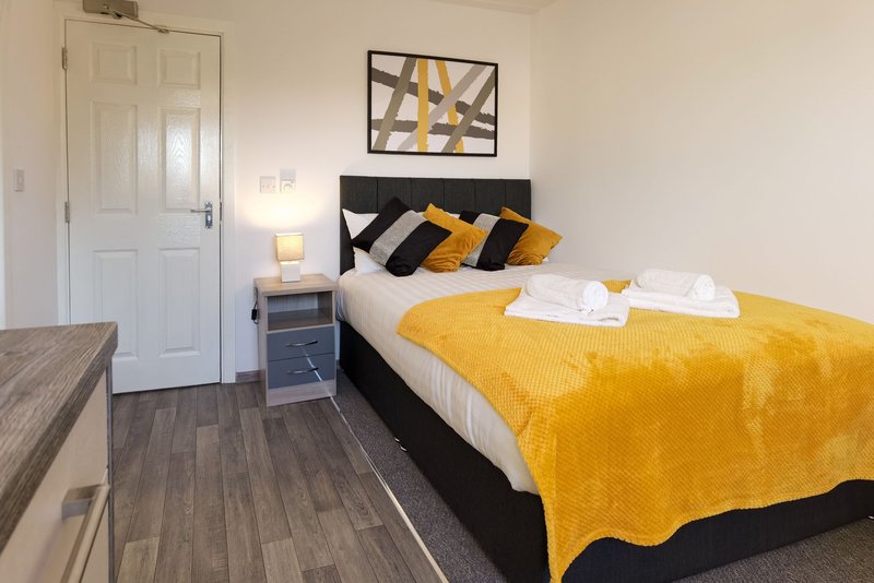 Bedroom with double bed, yellow bedding, black pillows, wooden flooring and wall art