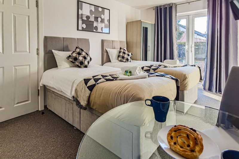 Modern twin bedroom with two beds, purple curtains, wall art, and small seating area