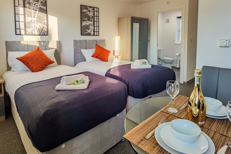 Twin bedroom with purple quilts, orange cushions, and dining table with wine bottle