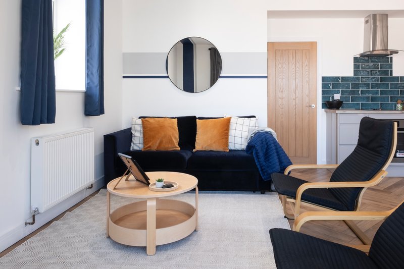 Modern living room with black sofa, wooden armchairs, round coffee table and circular mirror