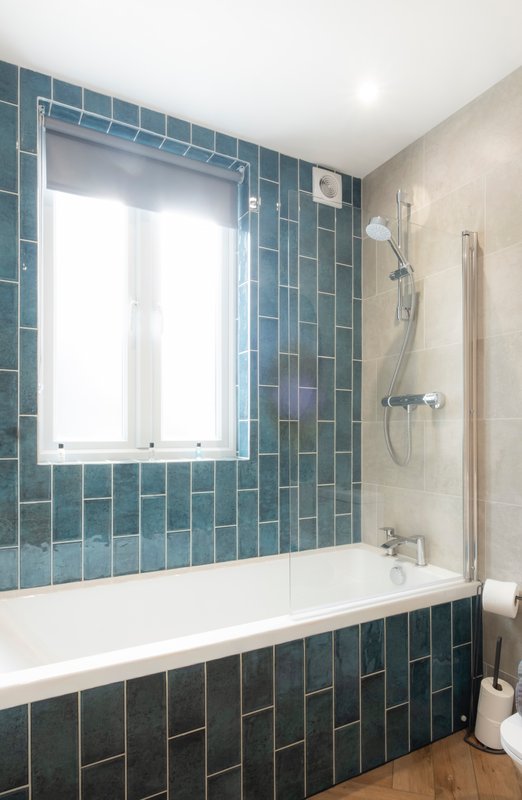 Modern bathroom with teal tile walls, white bathtub, window and shower fixtures