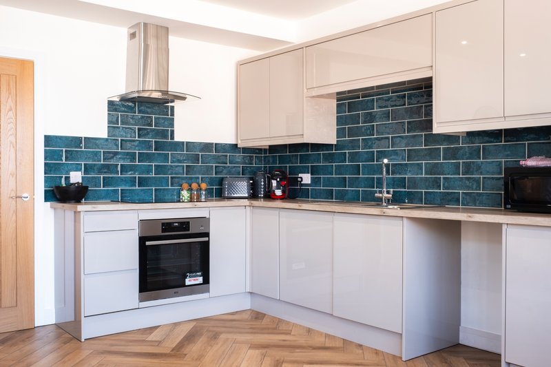 Modern kitchen with white cabinetry, blue tile backsplash, built-in oven and wooden flooring