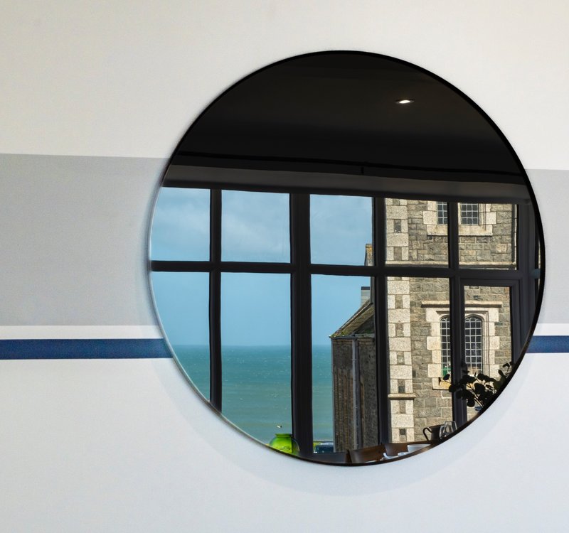 Circular mirror reflecting sea view, coastal building and blue-striped wall