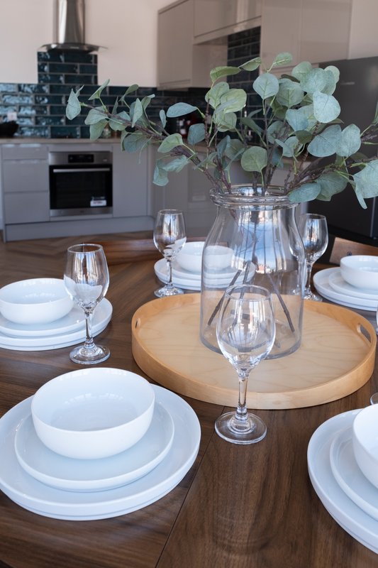 Dining table set with white plates, glasses, and eucalyptus centerpiece in kitchen
