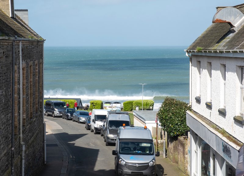 Coastal street view with parked vans, white-rendered buildings, and sea horizon beyond