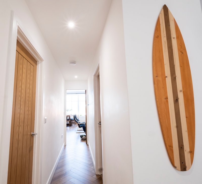 Bright hallway with wooden doors, white walls, and wooden surfboard wall art