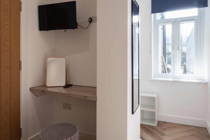 Small alcove with wall-mounted TV, shelf, stool, and window with bright natural light