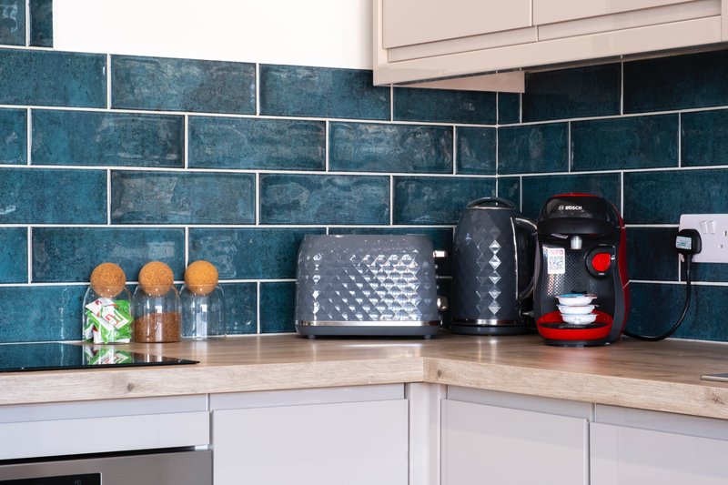 Modern kitchen with teal subway tile backsplash, white cabinets, wooden countertop and small appliances