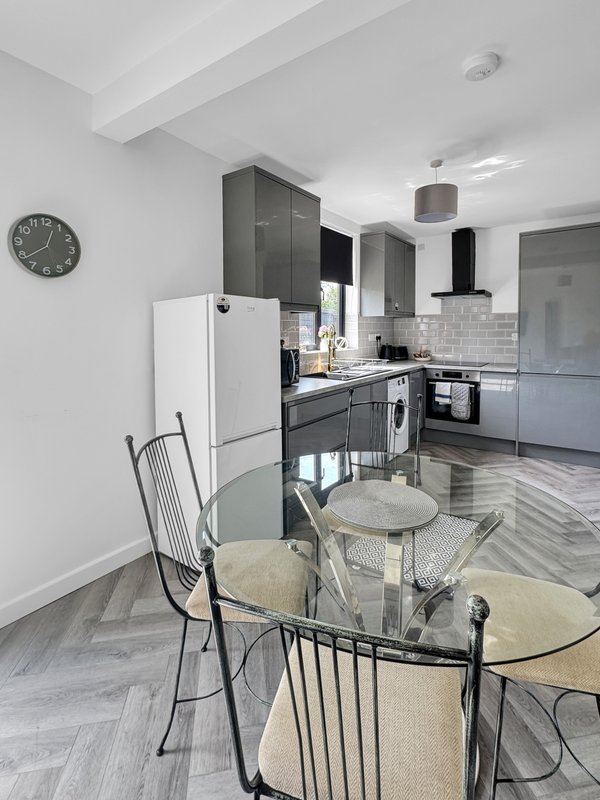 Modern kitchen and dining area with black cabinetry, white appliances, dining table and wall clock