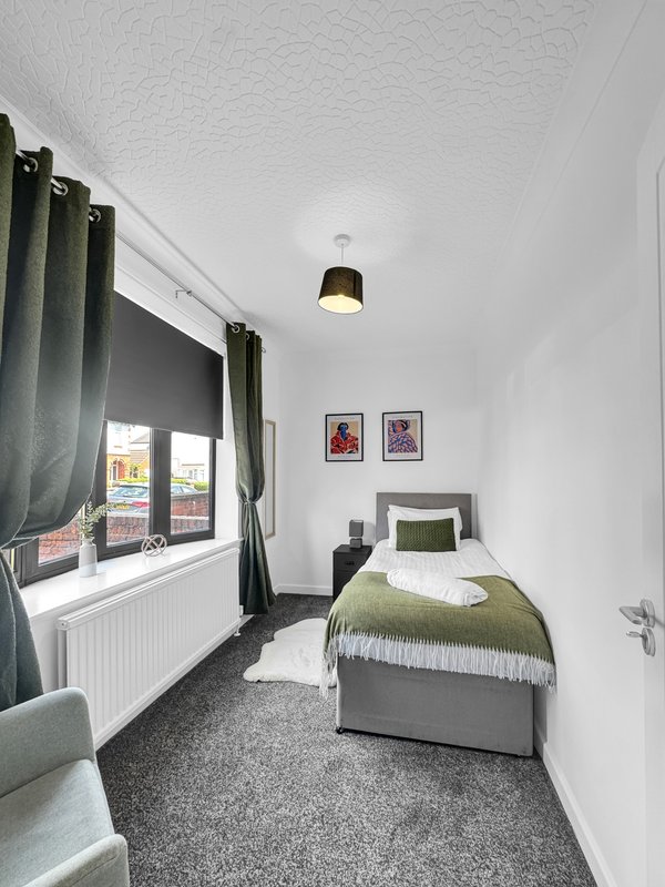 Compact bedroom with single bed, green bedding, dark curtains, pendant light and framed wall art