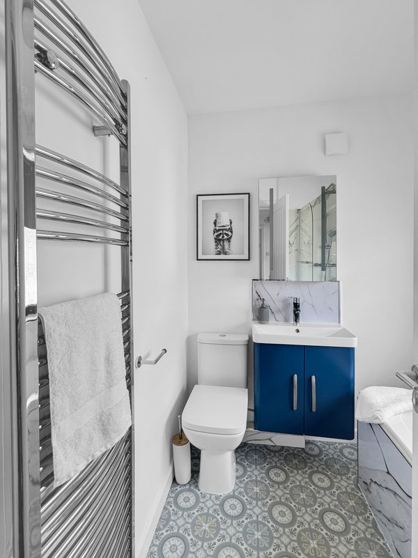 Modern bathroom with heated towel rack, blue vanity cabinet, toilet and patterned floor tiles