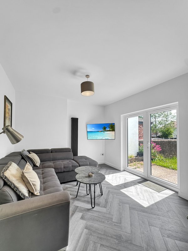 Modern living room with grey sectional sofa, glass doors to garden, mounted TV and ceiling lamp