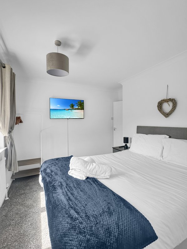 Bright modern bedroom with double bed, blue throw, wall-mounted TV, and ceiling lamp