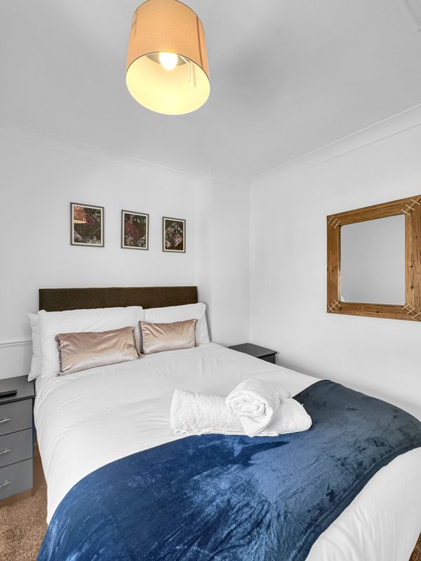 Modern bedroom with double bed, blue duvet, white pillows and wooden ceiling lamp