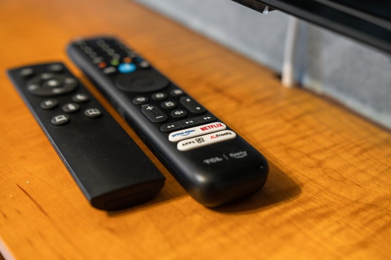 Two remote controls on wooden surface with warm lighting