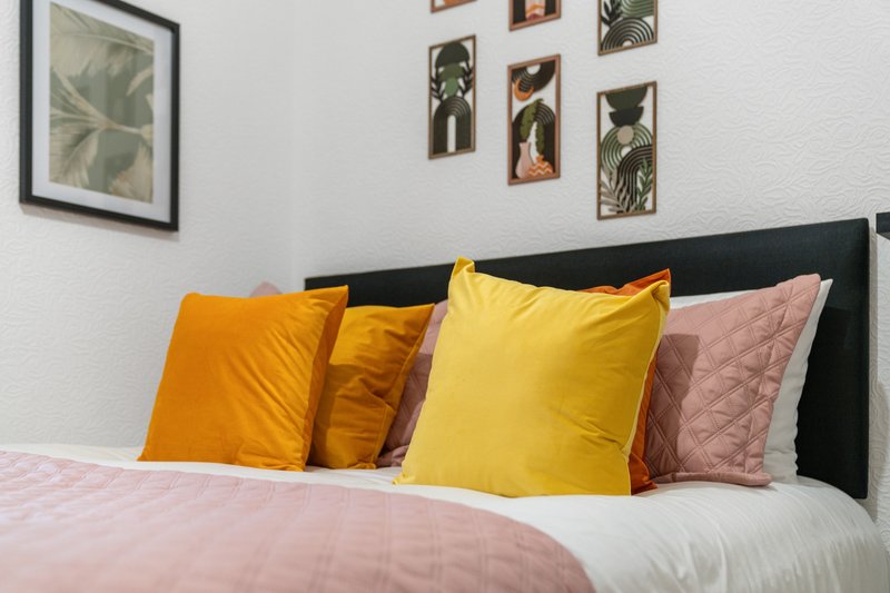Bedroom with black headboard, colorful cushions, and botanical wall art