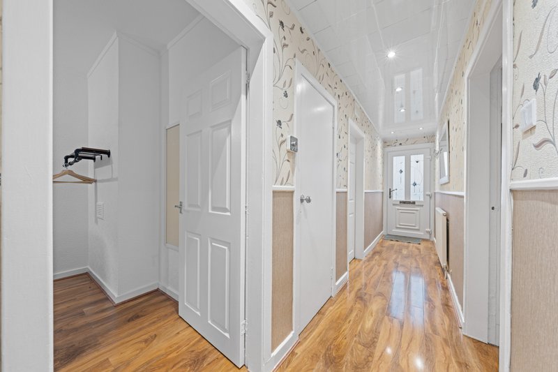 Long hallway with white paneled doors, wooden flooring, and neutral wall decor