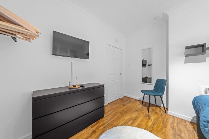 Modern bedroom with black dresser, wall-mounted TV, blue chair and wooden flooring