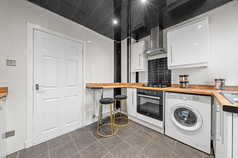 Modern kitchen with white cabinets, wooden countertops, black range hood, washing machine and built-in oven