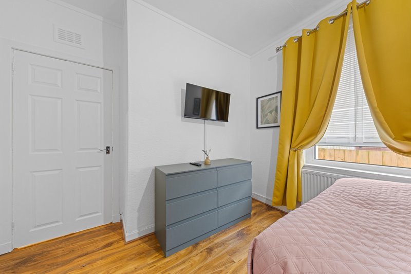 Bright bedroom with double bed, grey dresser, wooden floor and yellow curtains