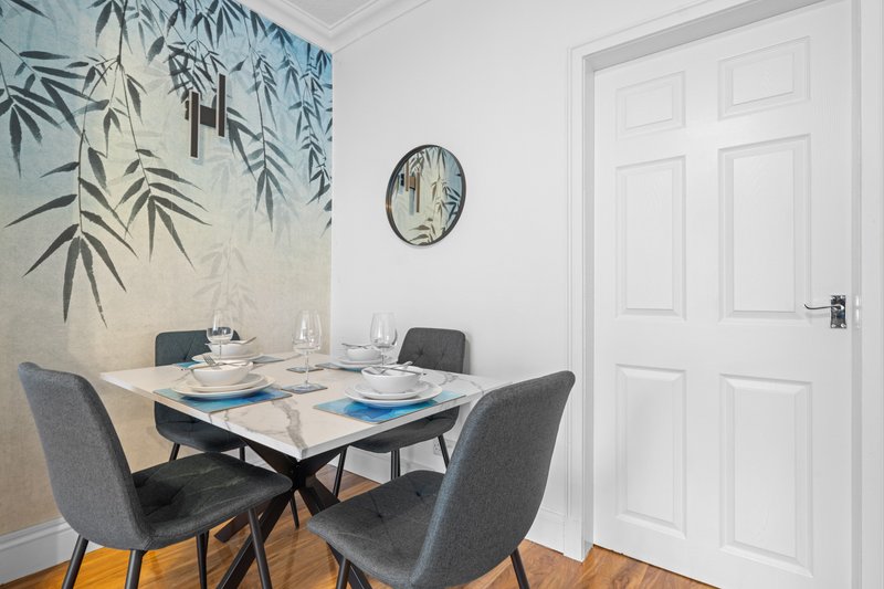 Dining area with square table, four grey chairs, and bamboo leaf wall art