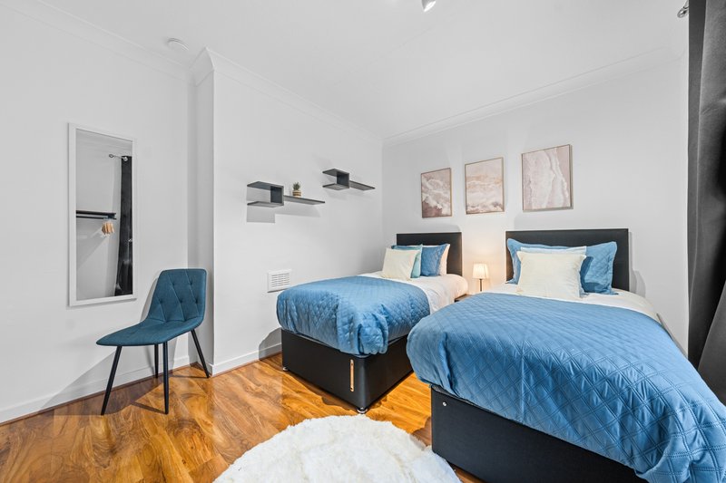 Modern twin bedroom with blue bedding, wooden floor, wall art and desk chair