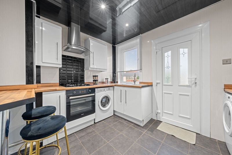 Modern kitchen with white cabinetry, wooden countertops, integrated appliances and breakfast bar seating