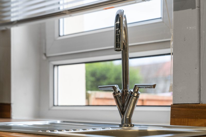 Modern kitchen sink with chrome tap and wooden countertop near bright window