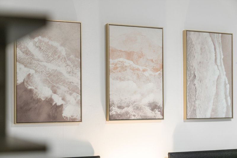 Three framed abstract landscape prints hanging on white wall above dark furniture