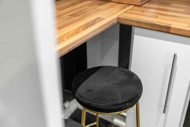 Kitchen counter with wooden top and black upholstered stool with brass legs
