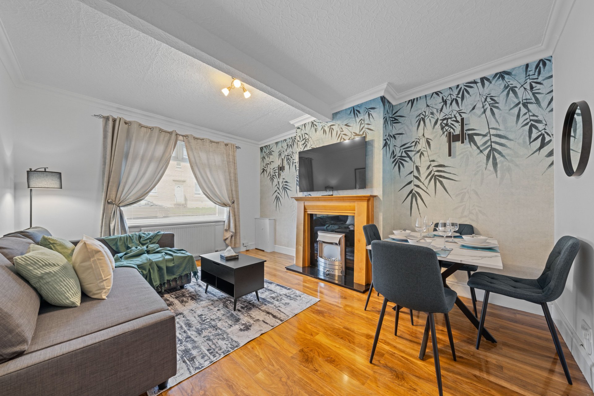 Open-plan living and dining area with sofa, fireplace, desk, and botanical wallpaper