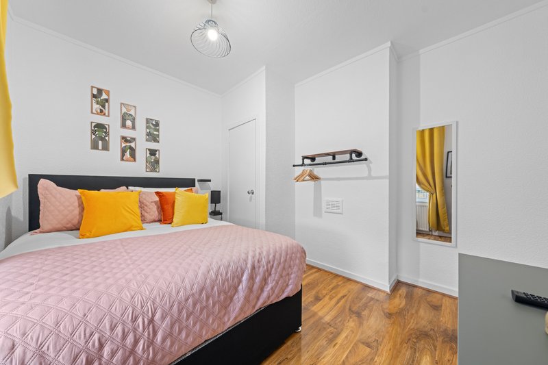 Bright bedroom with double bed, pink bedding, yellow and coral cushions, framed wall art