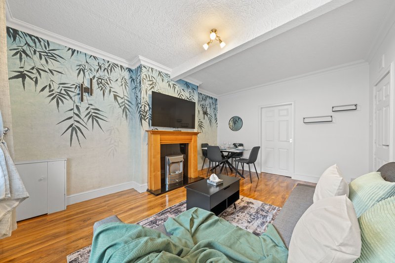 Living room with wooden fireplace, TV, sofa, and botanical wall mural decor