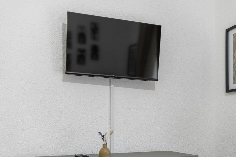 Wall-mounted flat-screen TV above shelf with small vase and flowers