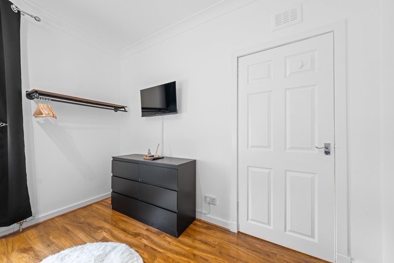Modern bedroom with dark chest of drawers, wall-mounted TV, wooden floor and white door