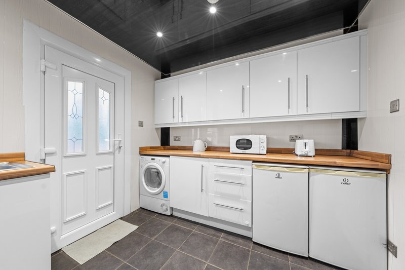 Modern kitchen with white cabinetry, wooden countertop, stainless steel appliances and washing machine